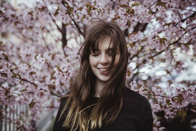 Portrait of smiling young woman standing by cherry tree