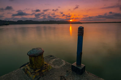 Wooden post in lake against sky during sunset