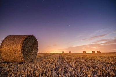 Hay bales on grassy field against sky at sunset
