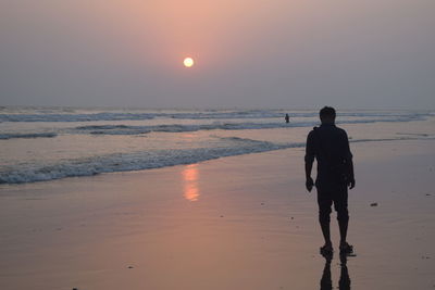 Rear view of silhouette man walking on beach at sunset