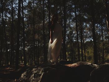 Rear view of woman standing by trees in forest