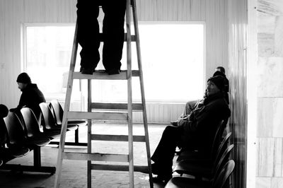 Low section of man on ladder by people sitting in waiting room