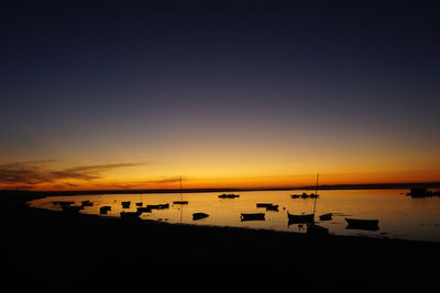 Silhouette boats in sea at sunset