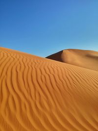 Scenic view of sand dunes in desert against clear blue sky