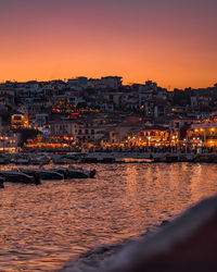 Illuminated buildings by sea against sky during sunset