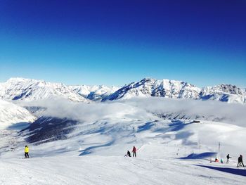 Tourists on snow covered mountain against clear sky