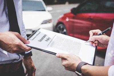 Midsection of customer signing contract while insurance agent holding clipboard