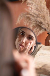 Mirror reflection of woman applying under-eye patch at dressing table closeup