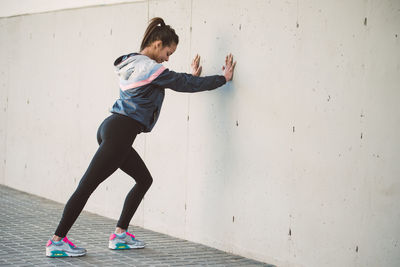 Full length of woman exercising while leaning on wall