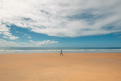 Rear view of woman walking at beach against sky