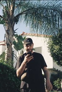Portrait of young man standing by palm tree
