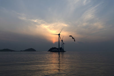 Silhouette cranes in sea against sky during sunset