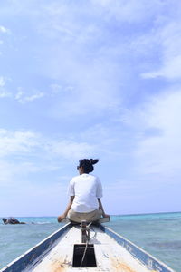 Rear view of man sitting on boat in sea against sky