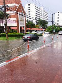 Wet road by city against sky