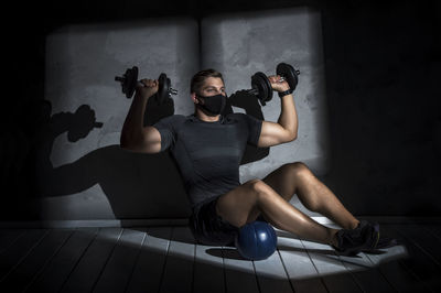 Full length of man wearing mask while exercising at gym