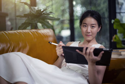 Portrait of woman using digital tablet while relaxing on sofa at home