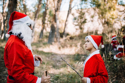Side view of mother and son wearing santa costume standing in forest
