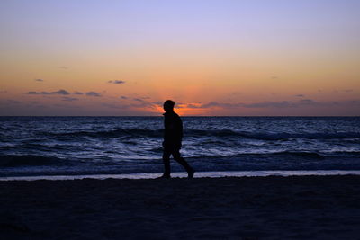 Silhouette man standing on beach against sky during sunset