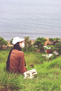 Rear view of woman sitting on field against sea