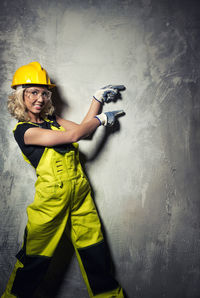 Portrait of smiling female worker pointing at concrete wall