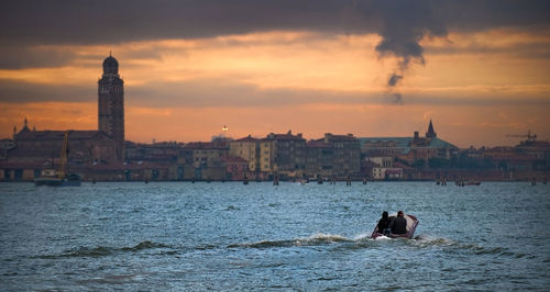 People jet boating in river against cityscape during sunset