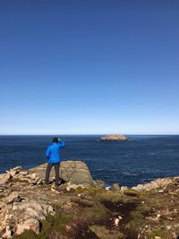 Woman standing on rock by sea against blue sky