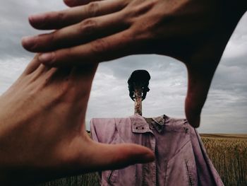 Cropped image of hand against scarecrow in field