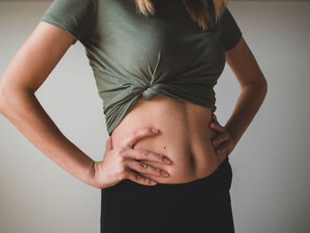 Midsection of woman touching face against gray background