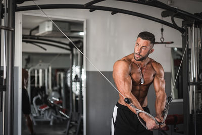 Full length of shirtless man with arms outstretched working out gym