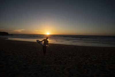 Silhouette female surfer walking at beach during sunset