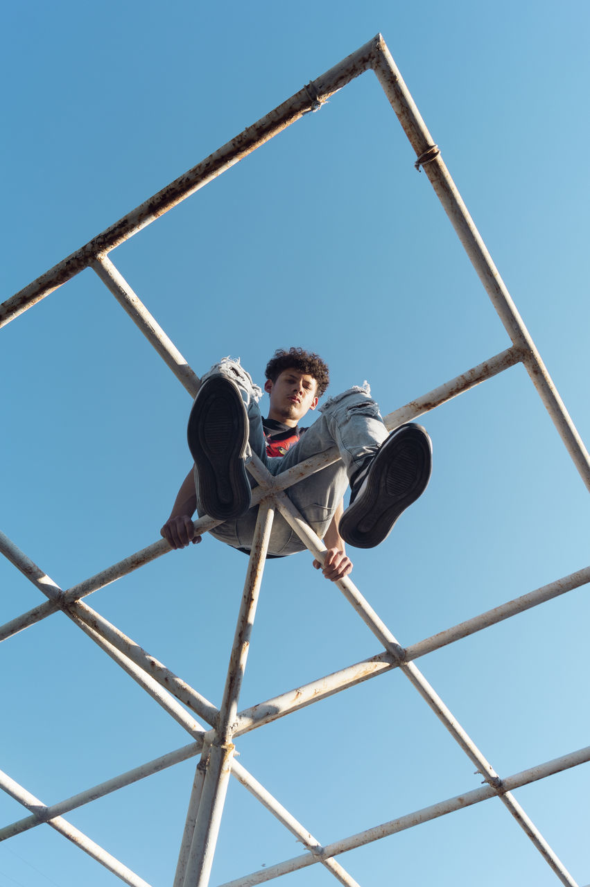 low angle view, sky, one person, real people, clear sky, nature, leisure activity, blue, casual clothing, day, full length, metal, child, men, young men, males, boys, lifestyles, outdoors, jungle gym, teenager, teenage boys