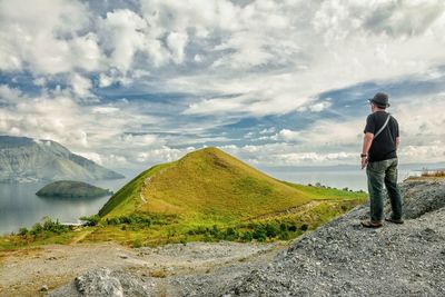 Man standing on rock looking at mountains against sky