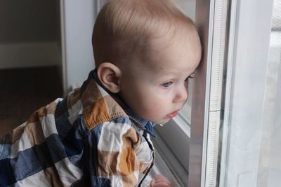 Side view of cute baby boy looking through window at home