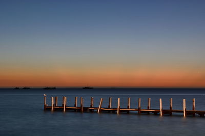 Wooden posts in sea against sky during sunset