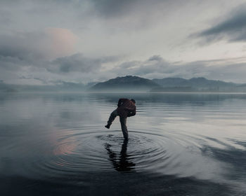 Rear view of man standing in lake against cloudy sky