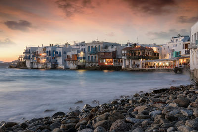 Buildings by sea against sky during sunset