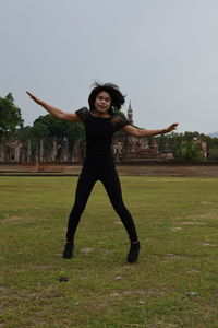 Full length of smiling young woman with arms raised on field