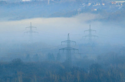 High voltage line in the alps in winter, foggy landscape