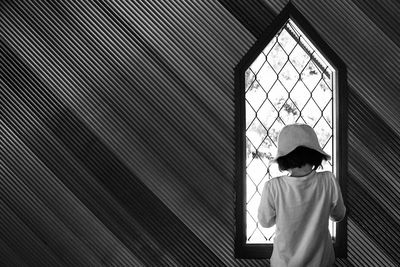 Rear view of girl standing against window at home