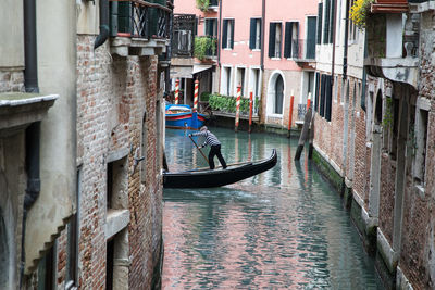 Gondolier sailing gondola in city amidst buildings