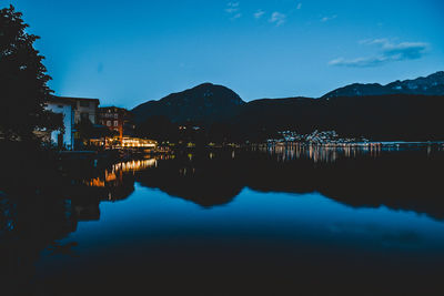 Scenic view of lake by illuminated city against sky at night