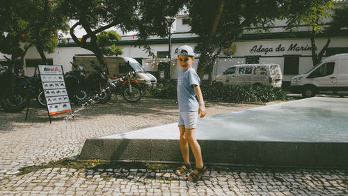 Boy standing by fountain against trees