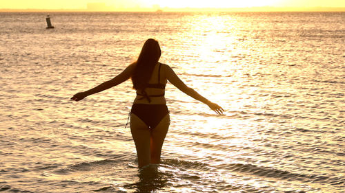 Rear view of woman standing at beach during sunset