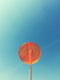 Low angle view of orange lollipop against clear blue sky