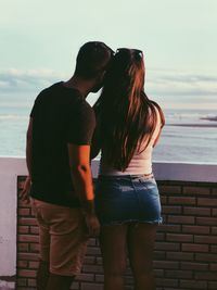 Rear view of couple standing at sea shore against sky