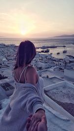 Rear view of woman sitting on beach against sky during sunset