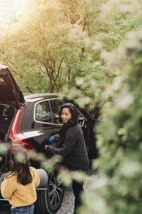 Young woman sitting by car on tree