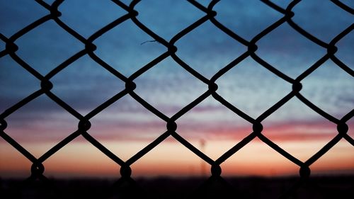 Full frame shot of chainlink fence against sky during sunset