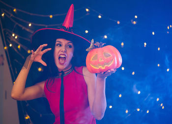 Portrait of happy woman with hat standing against illuminated lights