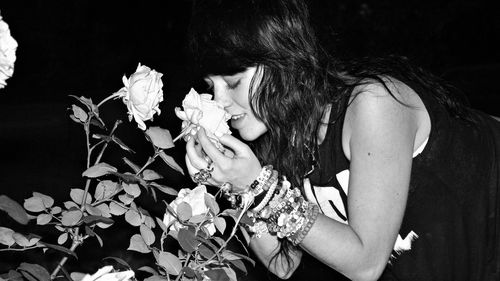 Midsection of woman holding flowering plant against black background